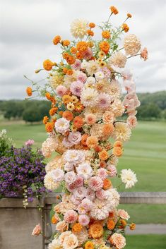 a tall vase filled with lots of flowers on top of a lush green grass covered field