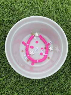 a white bowl filled with pink and white buttons on top of green grass next to a pair of scissors