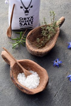 two wooden spoons filled with sea salt next to a bag of salt and flowers