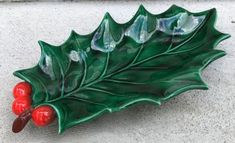 a ceramic holly leaf with red berries on it's side sitting on the ground