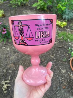 a person holding up a pink cup with an libra label on the inside and outside