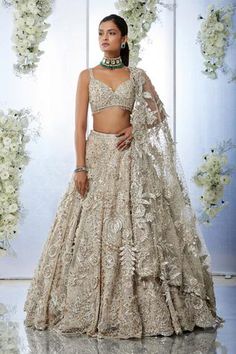 Beige lehenga features three-dimensional floral, sequin, pearl and crystal embroidery. Paired with a sweetheart neck blouse and a jaal embroidered net dupatta. 
Component: 3
Pattern: Embroidered
Type Of Work: Floral
Neckline: Sweetheart
Sleeve Type: Sleeveless
Fabric: Net
Color: Beige
Other Details: 
Floral embroidery
Tassel detail
Back tie-up
Embroidered dupatta
Occasion: Wedding, Bride - Aza Fashions Gold Reception Lengha, Reception Lengha Bridal, Shaadi Lehnga, Nude Lehenga, Reception Lengha, Gold Lengha, Hall Construction, Beige Lehenga, Sweetheart Neck Blouse