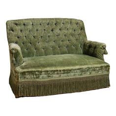 a green velvet couch with fringe trim on the arms and back, sitting in front of a white background