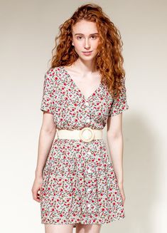 a young woman with red hair wearing a dress and heels standing in front of a white wall