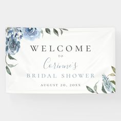 a welcome sign with blue flowers and greenery is hanging on a wall in front of a white background