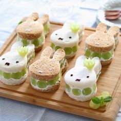 small sandwiches with green and white toppings are arranged on a wooden tray, ready to be eaten