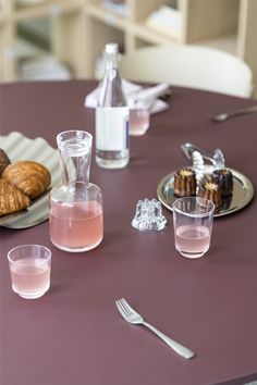 a table topped with plates and glasses filled with drinks next to croissants