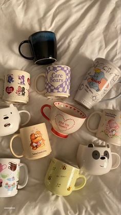 there are many coffee mugs on the bed and one is filled with cartoon characters