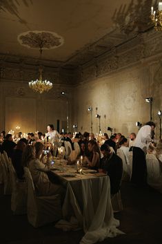 a group of people sitting at tables in a room with chandeliers on the ceiling