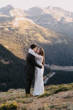 a bride and groom kissing on top of a mountain with mountains in the back ground