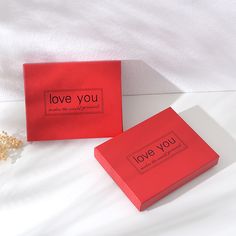 two red boxes sitting on top of a bed next to each other with the words love you written on them