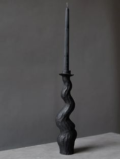 a tall black candle sitting on top of a white table next to a gray wall