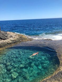 a person swimming in the ocean near some rocks and blue water with waves coming up on them