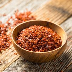 a wooden bowl filled with red chili flakes on top of a wooden table next to a spoon