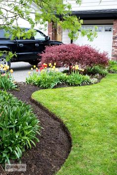 a black truck parked in front of a lush green yard with flowers and plants around it