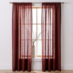 a window with red sheer curtains and a vase on the floor in front of it