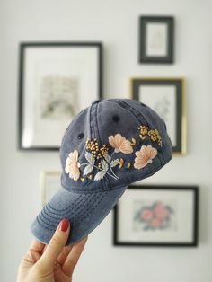 a woman's hand holding up a blue hat with embroidered flowers on the front