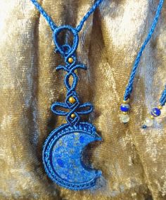 a blue and gold necklace with a crescent moon on the front hanging from it's side