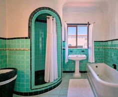 a green tiled bathroom with a tub, sink and toilet in it's corner