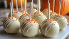 cake pops with white and orange sprinkles are on a plate next to pumpkins