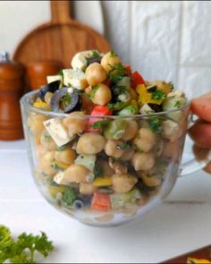 a glass bowl filled with chickpeas and vegetables on top of a white table