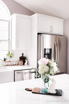 a vase with flowers sitting on top of a kitchen counter next to a refrigerator freezer