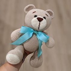 a hand holding a small crocheted teddy bear with a blue ribbon around its neck