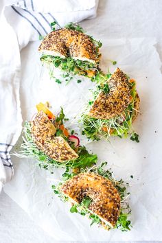 four sandwiches with sprouts and other toppings sitting on top of white paper