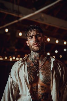 a man with tattoos on his chest wearing a white shirt and some lights in the background