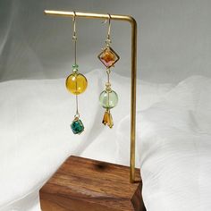 two different colored glass beads are hanging from gold earwires on a wooden stand