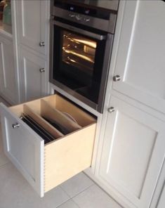 an open drawer in the middle of a kitchen with white cupboards and drawers on both sides