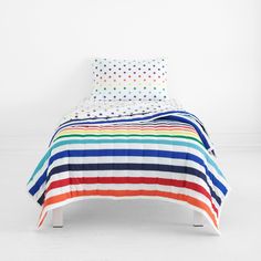 a bed with multicolored stripes and polka dots on the cover is in a white room