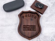 a wooden police badge next to a pair of sunglasses and a cell phone on a white surface