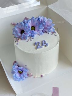 a white cake with purple flowers on top and the number twenty four in blue icing