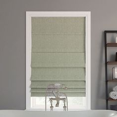 a bath tub sitting next to a window covered in roman shades