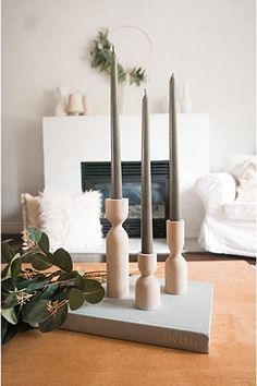 three candles are sitting on top of a book in front of a fireplace with greenery