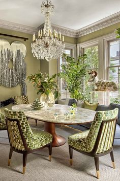 a dining room with green chairs and a marble table surrounded by potted plants in the center