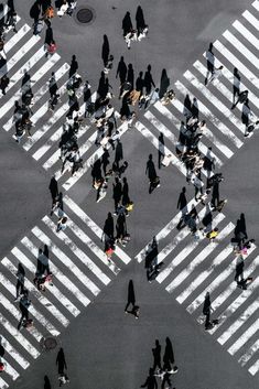 many people are walking across the crosswalk in this aerial photo, with shadows on the ground