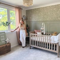 a woman standing next to a baby's crib in a room with floral wallpaper