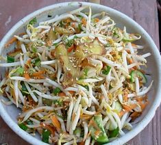 a white bowl filled with vegetables and sprouts on top of a wooden table