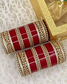 two red and gold bangles sitting on top of a table next to a golden box