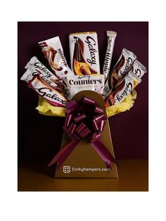 a box filled with assorted chocolates on top of a wooden table next to a purple ribbon