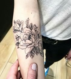 a woman's arm with a black and white flower tattoo on the left forearm