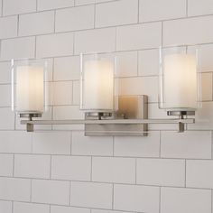 a bathroom light with three candles on the wall next to a white brick wall behind it