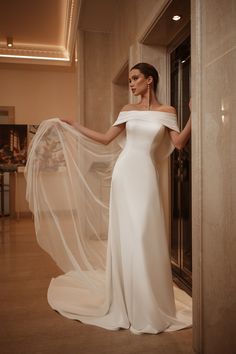 a woman in a white wedding dress is posing for the camera with her veil flowing over her shoulder