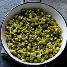 a pan filled with cooked green vegetables on top of a blue table cloth next to a knife