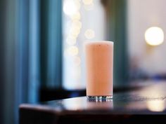 a tall glass filled with liquid sitting on top of a wooden table next to a window