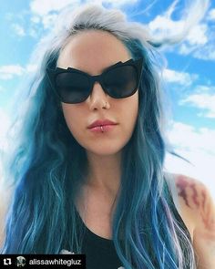 a woman with blue hair and black sunglasses posing for a photo in front of the sky