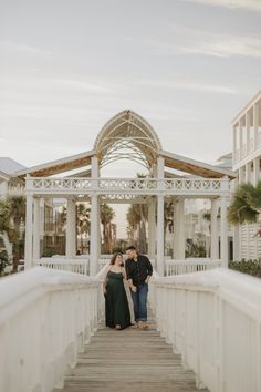 a man and woman standing on a bridge in front of some white buildings with palm trees