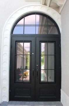 a black double door with two sidelights and arched glass on the front of a house